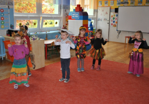 Dzieci stoją rozproszone na dywanie i tańczą taniec "kaczuszki". Ujęcie 1